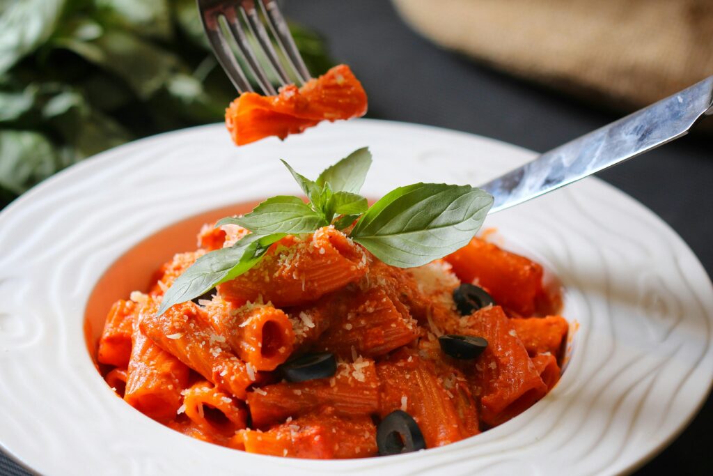 Delicious rigatoni pasta with tomato sauce, olives, and fresh basil, perfectly captured in a food photography shot.